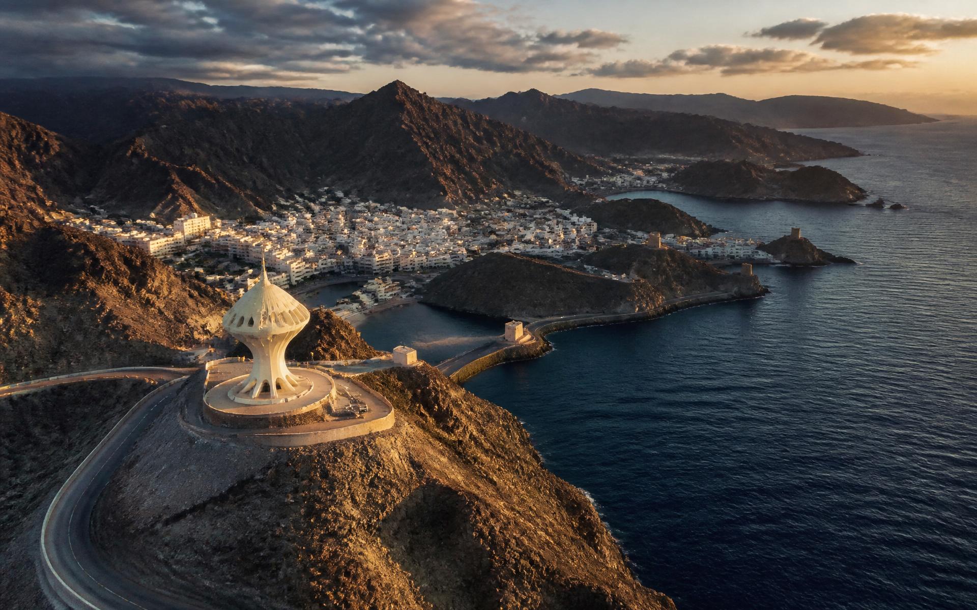 Aerial view of Muscat at golden hour with the Al Hajar mountains meeting the Sea of Oman.